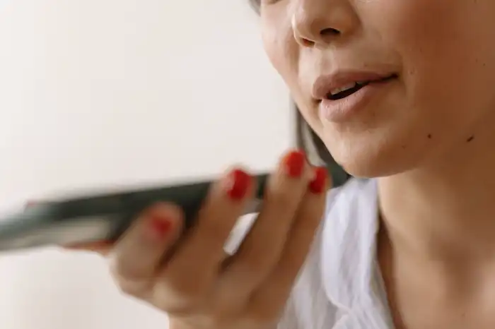 Kéz tartja a telefont a szájhoz közel, hangfelvétel készítése telefonnal otthon